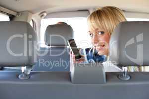 young blond woman with a smartphone on a backseat of a car