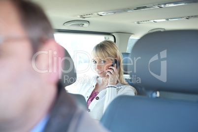 young blond woman with a smartphone on a backseat of a car