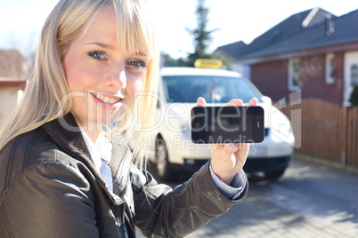 young blond woman with smartphone and taxicab