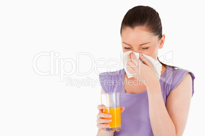 Good looking woman holding a glass of orange juice and sneezing