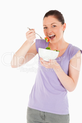 Good looking woman eating a bowl of salad while standing