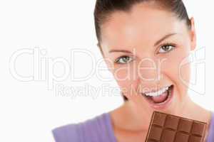 Portrait of a pretty woman eating a chocolate block while standi