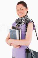 Charming student holding books and her bag while standing