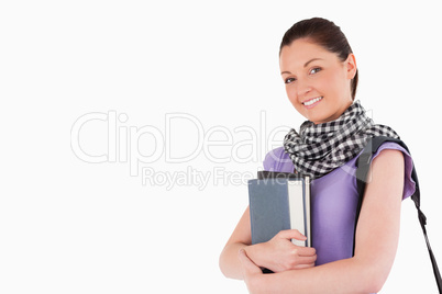 Good looking student holding books and her bag while standing