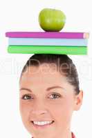 Beautiful female holding an apple and books on her head while st