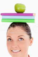 Attractive female holding an apple and books on her head while s