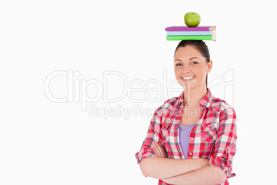 Pretty female holding an apple and books on her head while stand