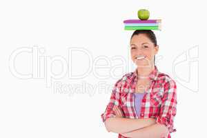 Pretty female holding an apple and books on her head while stand