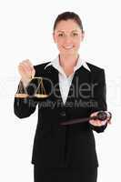 Charming woman in suit holding scales of justice and a gavel while standing against a white background