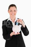 Charming woman in suit inserting a money bill in a pink piggy ba