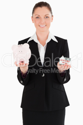 Good looking woman in suit holding a piggy bank and a miniature