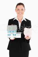 Pretty woman in suit holding a piggy bank and a miniature house