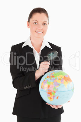 Charming female in suit holding a globe and using a magnifying g