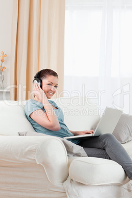 Good looking woman with headphones relaxing with her laptop whil