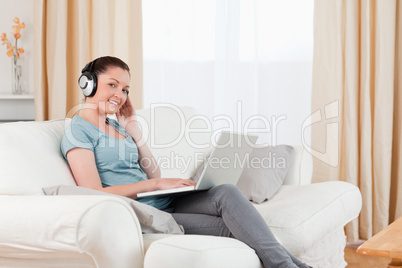 Pretty woman with headphones relaxing with her laptop while sitt