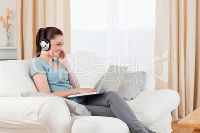 Gorgeous woman with headphones relaxing with her laptop while si