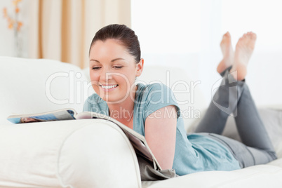 Charming woman reading a magazine while lying on a sofa