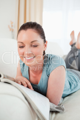Lovely female reading a magazine while lying on a sofa