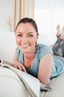 Cute woman reading a magazine while lying on a sofa
