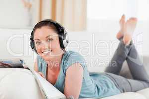 Cute woman with headphones reading a magazine while lying on a s