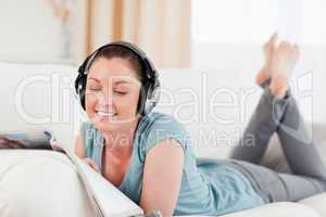 Lovely woman with headphones reading a magazine while lying on a