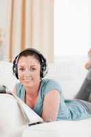 Beautiful woman with headphones reading a magazine while lying o