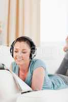Attractive woman with headphones reading a magazine while lying