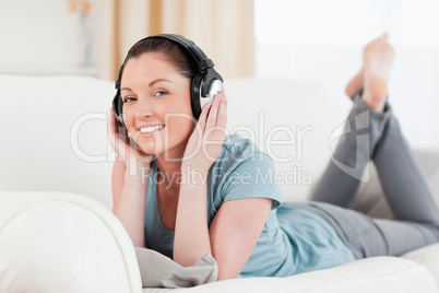 Charming woman with headphones posing while lying on a sofa