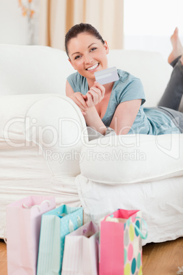 Beautiful woman holding her credit card and posing while lying o