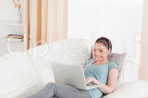 Lovely woman relaxing with her laptop while lying on a sofa