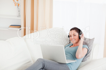 Gorgeous female with headphones relaxing on her laptop while lyi