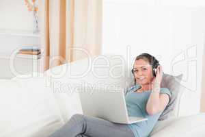 Gorgeous female with headphones relaxing on her laptop while lyi