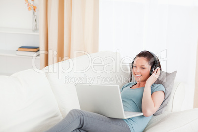 Beautiful female with headphones relaxing on her laptop while ly