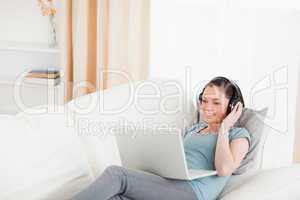 Beautiful female with headphones relaxing on her laptop while ly