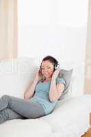 Attractive female using headphones while lying on a sofa