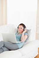 Attractive female with headphones relaxing on her laptop while l