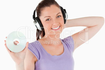 Charming woman with headphones holding a CD while standing