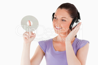 Good looking female with headphones holding a CD while standing