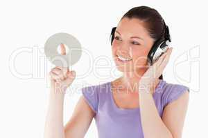 Good looking female with headphones holding a CD while standing