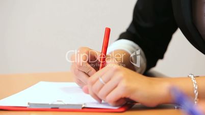 Eine Frau schreibt mit Kugelschreiber auf einem Klemmbrett
