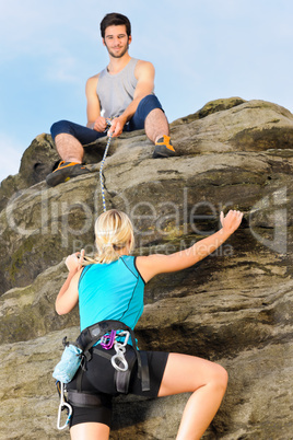 Woman climbing up rock man hold rope