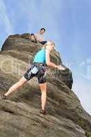 Woman climbing up rock man hold rope