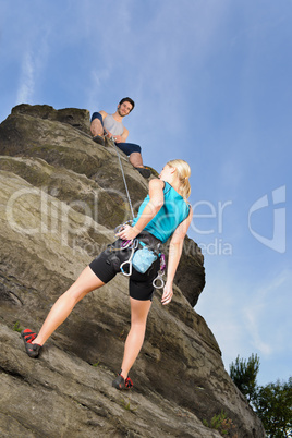 Woman climbing up rock man hold rope