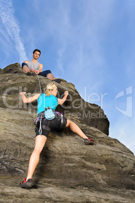 Woman climbing up rock man hold rope