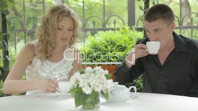 Beautiful young couple drinking tea in summer cafe and talking