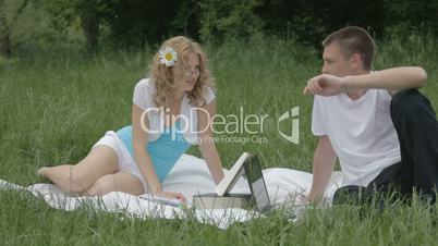 Cheerful young couple discussing something with opened book and laptop
