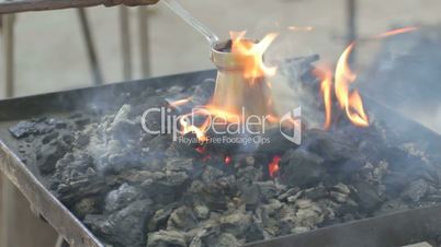 Flames rising above hot coals, covering pot with brewed coffee