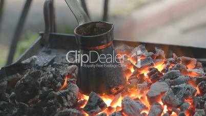 Charred pot with brewing coffee standing on fading embers