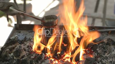 Preparing coffee in bronze pot outdoors on live coals