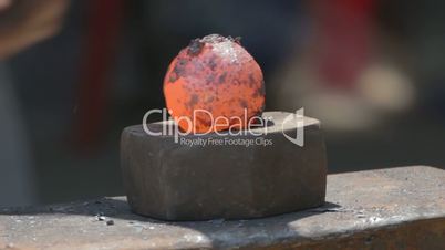 Blacksmith hammering hot round metal to shape it